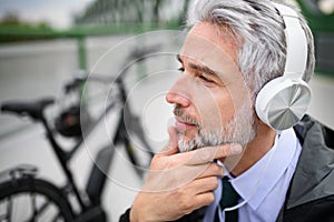 Businessman with bike sitting on bench, listening to music and resting. Commuting and alternative transport concept