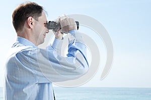 Businessman with binoculars against blue sky