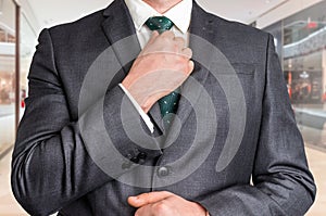 Businessman in black adjusting his tie in shopping center