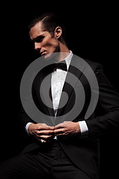 Businessman in black suit with bowtie posing seated in dark