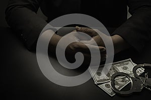 A businessman in a black suit, handcuffs on the table against the black table, hands the money to the police for release.