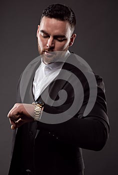 A businessman in a black suit looks at the time on his wristwatch