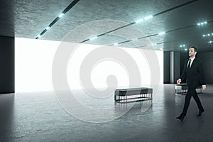 Businessman in black suit in a spacious modern hall with big blank white screen wall, concerete flloor and benches. Business