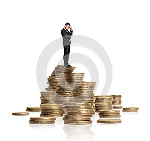 Businessman in black suit standing on heap of glittering golden coins isolated white background