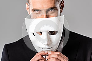 Businessman in black suit taking off white mask isolated on grey