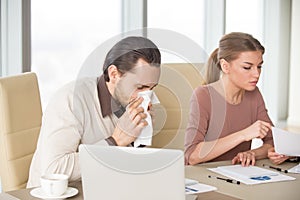 Businessman blowing nose working in office with colleagues, seas