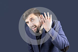 A businessman in a blue suit puts his hand to his ear, trying to hear something