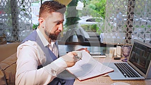 Businessman in blue vest drinks coffee and makes notes