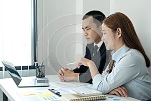 Businessman boss in suit explaining about new business project to her and woman office worker is pointing