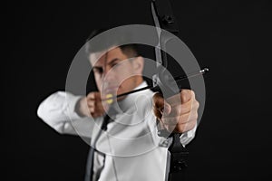 Businessman with bow and arrow practicing archery against black background, focus on hand