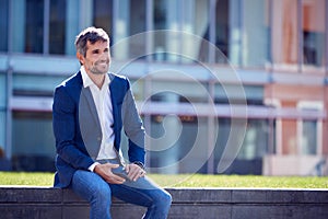 Businessman On A Break Sitting Outside Office Holding Mobile Phone