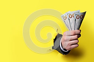 Businessman breaking through yellow paper with money in fist, closeup. Space for text