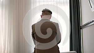 Businessman in brite hotel room puts on jacket, back view. unrecognizable man puts on strict jacket and prepares for