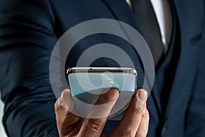 A businessman in a business suit holds a smartphone in his hands. Uses the Internet to work and communicate with partners. Online