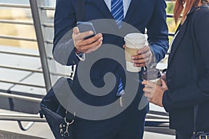 Businessman Businesswoman drinking coffee in town using smartphone outside office modern city. Hands holding take away coffee cup