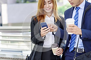 Businessman Businesswoman drinking coffee in town using smartphone outside office modern city. Hands holding take away coffee cup