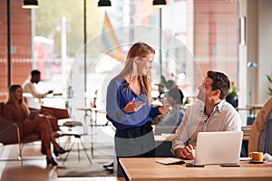 Businessman And Businesswoman Having Informal Meeting By Desk In Modern Open Plan Office
