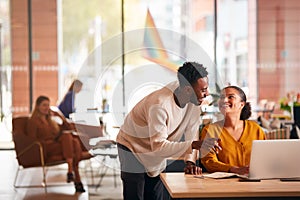 Businessman And Businesswoman Having Informal Meeting By Desk In Modern Open Plan Office