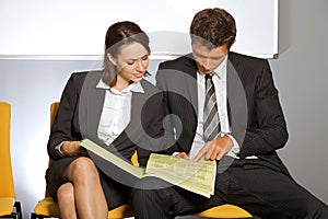 Businessman and businesswoman reading newspaper at waiting room