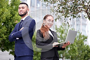 Businessman and businesswoman realtors with laptop outside, asian kazakh entrepreneurs discuss project