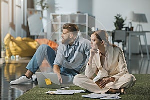 Businessman and businesswoman sitting on floor and using laptop