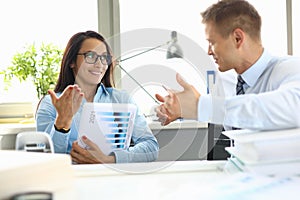 Businessman and businesswoman are sitting at table in office having dialogue.