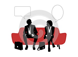 Businessman and businesswoman speaking seated on red sofa