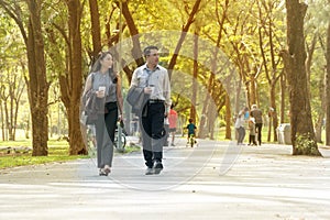 Businessman and businesswoman walking together within the park relaxed after work. Two businessmen holding cup of coffee