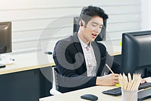 Businessman Call Center and technical Support staff with headset talking and writing in yellow paper note for job. Asian customer