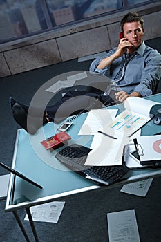 Businessman on call feet up papers all around