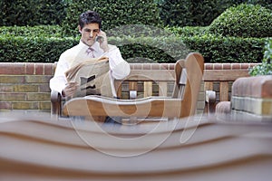 Businessman On Call While Reading Newspaper In Park