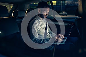 Businessman in car working on laptop in back seat