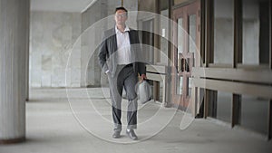 Businessman carrying briefcase while moving forward. Man in formalwear walking near modern office building, full length