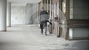 Businessman carrying briefcase while moving forward. Man in formalwear walking near modern office building, full length