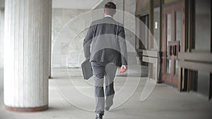 Businessman carrying briefcase while moving forward. Man in formalwear walking near modern office building, full length