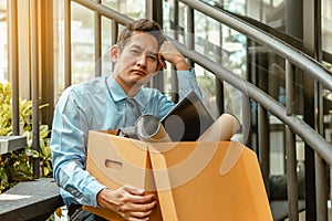 Businessman is carrying a brown cardboard box to resignation. Depressed Businessman sitting on ground stairs suffering emotional s