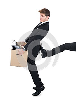 Businessman carrying cardboard box with leg kicking him