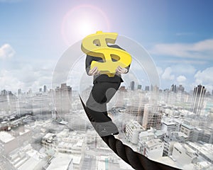 Businessman carrying gold dollar sign balancing on wire