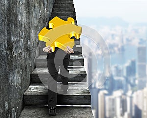 Businessman carrying gold puzzle piece climbing on old stairs