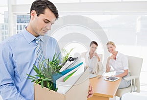 Businessman carrying his belongings with colleagues in background