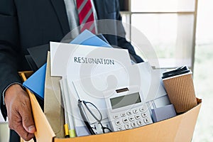 Businessman carrying packing up all his personal belongings and files into a brown cardboard box to resignation in modern office,