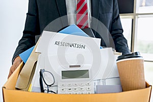 Businessman carrying packing up all his personal belongings and files into a brown cardboard box to resignation in modern office,