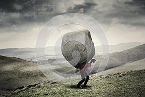 Businessman carrying rock at hill photo