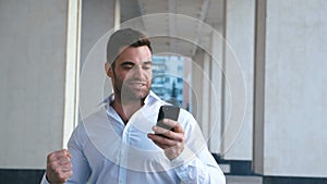 Businessman Celebrating Success while Reading Message in Smartphone near office building. Handsome professional