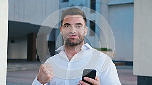 Businessman Celebrating Success while Reading Message in Smartphone near office building. Handsome professional