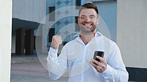 Businessman Celebrating Success while Reading Message in Smartphone near office building. Handsome professional