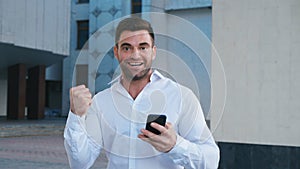 Businessman Celebrating Success while Reading Message in Smartphone near office building. Handsome professional