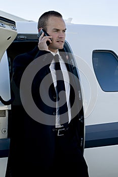 Businessman on cell phone exiting corporate jet