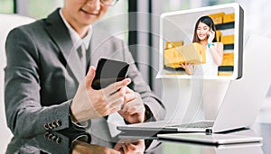 Businessman CEO order product box from young female Asian small business owner using phone, laptop. E-commerce technology concept