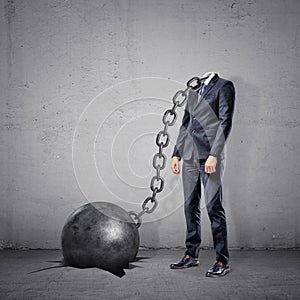 A businessman with a chain connected to a wrecking ball instead of his head stands on a concrete background.